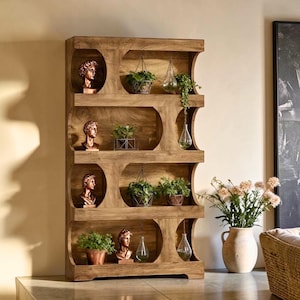 May include: A wooden bookshelf with a unique design, featuring curved cutouts and multiple shelves. The shelves display bronze busts, potted plants, and hanging glass terrariums, creating a decorative and functional storage unit.