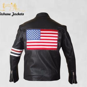 Könnte beinhalten: Schwarze Lederjacke mit einem amerikanischen Flaggenaufnäher auf dem Rücken. Die Jacke hat einen Reißverschluss und rot, weiß und blaue Streifen am linken Ärmel. Der Text "Stitchure Jackets" befindet sich oben.