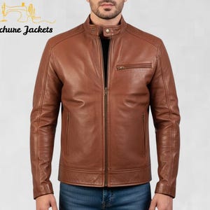May include: A brown leather jacket with a stand-up collar and a zipper closure. The jacket has a small chest pocket and is made of a smooth, textured leather. The logo "Stitchure Jackets" is in the upper left corner.