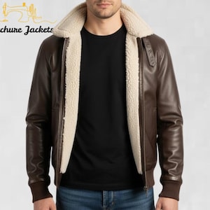 May include: A brown leather jacket with a cream-colored shearling lining and collar. The jacket has a zipper closure and ribbed cuffs. The text "Stitchure Jackets" is visible in the upper left corner.