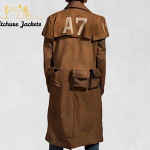 Può includere: Un lungo cappotto marrone con più tasche e un colletto a mantella. Il numero "A7" è stampato in bianco sul retro del cappotto. Il cappotto è di Stitchure Jackets.