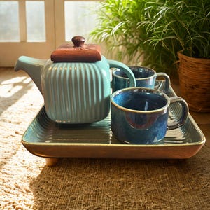 Pode incluir: Um conjunto de chá de cerâmica azul-turquesa com tampa de madeira e duas canecas a condizer assenta numa bandeja retangular. A bandeja tem base de madeira e pés pequenos. O conjunto de chá está sobre um tapete tecido.