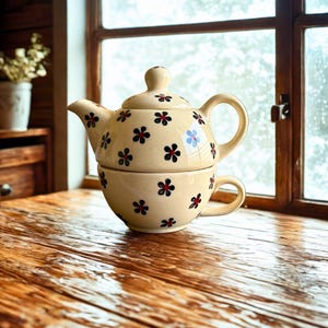 May include: A set of three ceramic mugs with a speckled, matte finish. The mugs are in shades of cream, light gray, and dark gray. Each mug has a simple, minimalist design and a rounded handle.