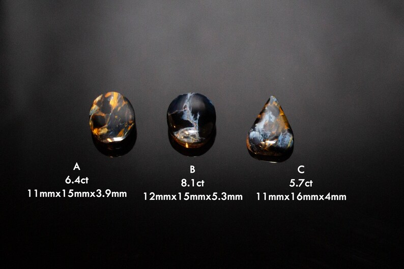 May include: Three blue and gold tiger's eye gemstones, labeled A, B, and C. Gemstone A is 6.4ct and measures 11mm x 15mm x 3.9mm. Gemstone B is 8.1ct and measures 12mm x 15mm x 5.3mm. Gemstone C is 5.7ct and measures 11mm x 16mm x 4mm.