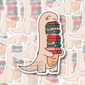 May include: A sticker featuring a smiling, light brown dinosaur carrying a stack of books. The books are in shades of red, pink, and green. The sticker has a white border and the text "Sugar & Starlight".