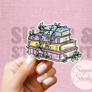 May include: A die-cut sticker featuring a stack of four books in pastel shades of blue, purple, yellow, and pink. A green vine with small leaves wraps around the books. The illustration has a black outline and a white border on a pink background.