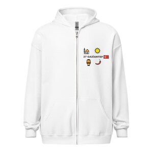 Könnte beinhalten: Weißer Kapuzenpullover mit Reißverschluss, Kapuze und Vordertaschen. Das Design auf der Brust umfasst eine Moschee, eine Sonne, eine Vase, eine Chilischote und die türkische Flagge sowie den Text "27 GAZIANTEP".