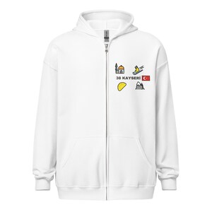 Könnte beinhalten: Weißer Kapuzenpullover mit Reißverschluss und einem kleinen Aufdruck auf der Brust. Der Aufdruck enthält den Text "38 KAYSERI" und mehrere farbenfrohe Illustrationen einer Moschee, eines Skifahrers, der türkischen Flagge und anderer Symbole.