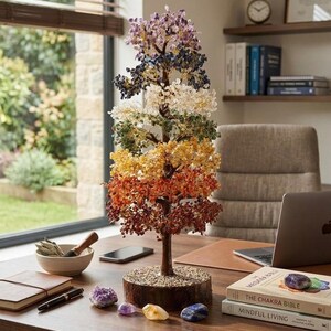May include: A decorative tree sculpture featuring branches adorned with multi-coloured gemstone chips arranged in layers of purple, blue, clear, green, yellow, orange, and red, set on a circular wooden base covered with small light-coloured pebbles.