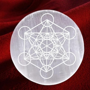 Può includere: Un piatto rotondo di cristallo di selenite traslucido con un disegno bianco del Cubo di Metatron inciso sulla superficie. Il motivo geometrico è composto da cerchi, linee e forme interconnesse. Sfondo rosso scuro.