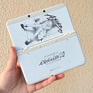 May include: A white Nintendo 3DS handheld game console, open to display a black and white character illustration. The lower section of the console features the text "GROUNDWORK OF EVANGELION 2.0 YOU CAN (NOT) ADVANCE."