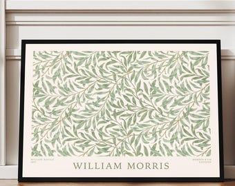 May include: A framed art print featuring a repeating pattern of green leaves on a cream background. The print is labeled "WILLIAM MORRIS" in black text. The artwork is displayed on a wooden floor, leaning against a white wall.