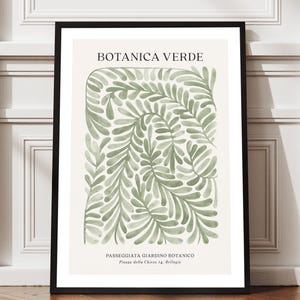 May include: A framed botanical print with the text "BOTANICA VERDE" and a watercolor illustration of green leaves. The print is displayed on a wooden floor against a white wall.