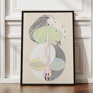 May include: Abstract art print in a black frame. The artwork features a complex design with geometric shapes and soft colors, including green, gray, pink, and white. The print is displayed against a neutral background.