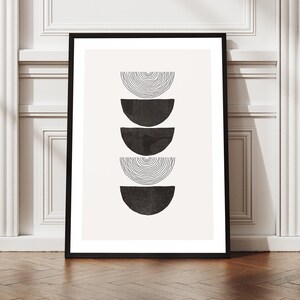 Könnte beinhalten: Gerahmter Kunstdruck mit minimalistischem Design. Er zeigt fünf gestapelte, halbkreisförmige Formen in Schwarz und schwarz linierten Mustern auf cremefarbenem Hintergrund. Das Kunstwerk wird auf einem Holzboden präsentiert. Der Rahmen ist schwarz.
