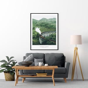 Pu&ograve; includere: Stampa artistica incorniciata con un treno su un ponte di pietra, con colline verdi sullo sfondo. La stampa ha il testo "Hogwarts Express" in basso. L'opera d'arte &egrave; esposta sopra un divano grigio e un tavolo di legno.