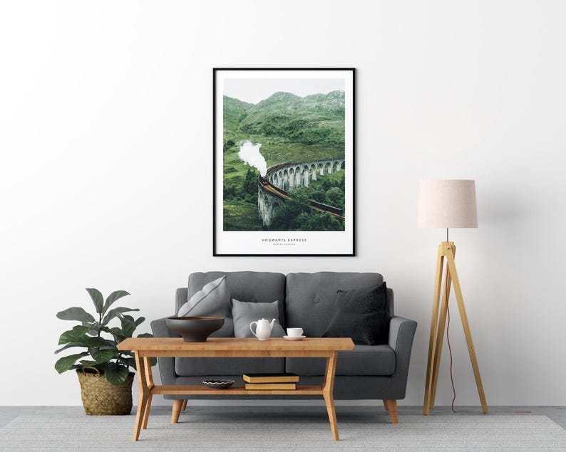 Pu&ograve; includere: Stampa artistica incorniciata con un treno su un ponte di pietra, con colline verdi sullo sfondo. La stampa ha il testo "Hogwarts Express" in basso. L'opera d'arte &egrave; esposta sopra un divano grigio e un tavolo di legno.