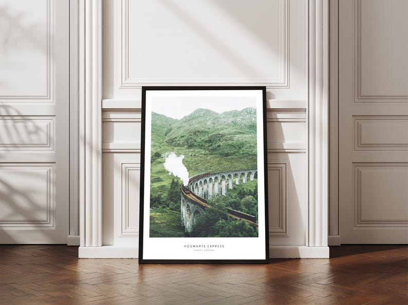 Pu&ograve; includere: Una stampa incorniciata raffigurante l'Hogwarts Express che attraversa un viadotto in pietra. L'immagine mostra un treno a vapore sullo sfondo di verdi colline e un cielo nuvoloso. La stampa &egrave; esposta su un pavimento in legno.