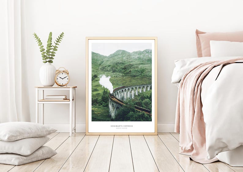 Pu&ograve; includere: Una stampa incorniciata del treno Hogwarts Express che attraversa il viadotto di Glenfinnan in Scozia. L'immagine mostra un treno a vapore su un ponte di pietra circondato da verdi colline. Il testo "Hogwarts Express" &egrave; in basso.