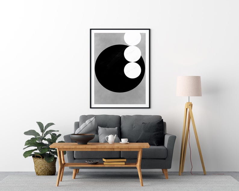 Op de afbeelding: Een ingelijste abstracte kunstprint met een groot zwarte cirkel en drie witte cirkels op een grijze achtergrond. Het kunstwerk hangt boven een grijze bank en past in een moderne woonkamer. De print zit in een zwarte lijst.