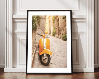 May include: Framed print featuring an orange vintage scooter parked on a cobblestone street. The scooter is positioned in front of a stone wall, with a narrow alleyway in the background. The image has a warm, sunny aesthetic, evoking a sense of travel and adventure.