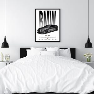 May include: A framed black and white poster featuring a BMW M4 G82 car. The BMW logo is prominently displayed above the car image. The poster is mounted on a white wall above a bed with white bedding.