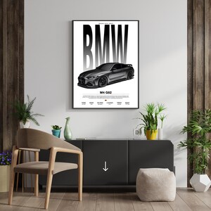 May include: A framed poster featuring a gray BMW M4 G82 car illustration. The poster has the BMW logo in large, bold, black letters. Below the car is the text "M4 G82" and other technical specifications.