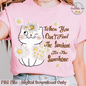 May include: Pink t-shirt featuring a white cat illustration adorned with daisy flowers. The cat winks and is surrounded by daisies. Text reads "When You Can't Find The Sunshine Be The Sunshine". The shirt is a digital download.