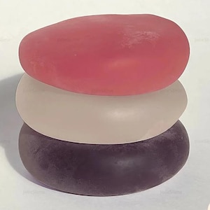 May include: A stack of three smooth, jelly-like sweets in shades of pink, beige, and purple. The top sweet is a bright pink, the middle is a pale beige, and the bottom is a dark purple. The sweets are stacked. The logo "Mochich! by Julie" is in the bottom right corner.