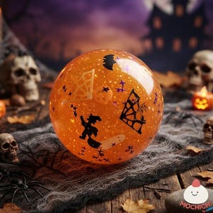 May include: A spherical orange glitter ornament featuring black silhouettes of a witch, a bat, and spider webs. The surface is filled with small star-shaped confetti. The object is positioned centrally, showcasing a festive Halloween-themed design.