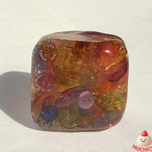 Pode incluir: Uma caneca de cerâmica branca com uma alça preta e o texto "But First, Coffee" em preto, com uma fonte manuscrita. A caneca está sobre uma superfície branca.