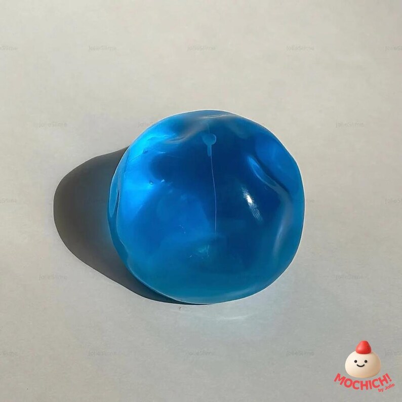 Op de afbeelding: Een helderblauwe, doorschijnende, bolvormige object met een glad oppervlak. Het object werpt een donkere schaduw op een lichtgrijze achtergrond. De afbeelding is goed verlicht en benadrukt de kleur en vorm van het object.