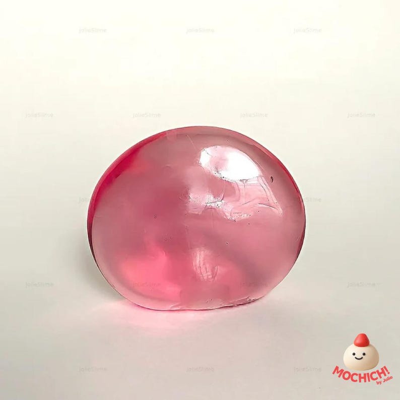 Op de afbeelding: Een doorzichtige, roze slijmbal ligt op een witte ondergrond. Het slijm is glad en bolvormig, met een glanzend uiterlijk. Het Mochich!-logo staat rechtsonder in de afbeelding.
