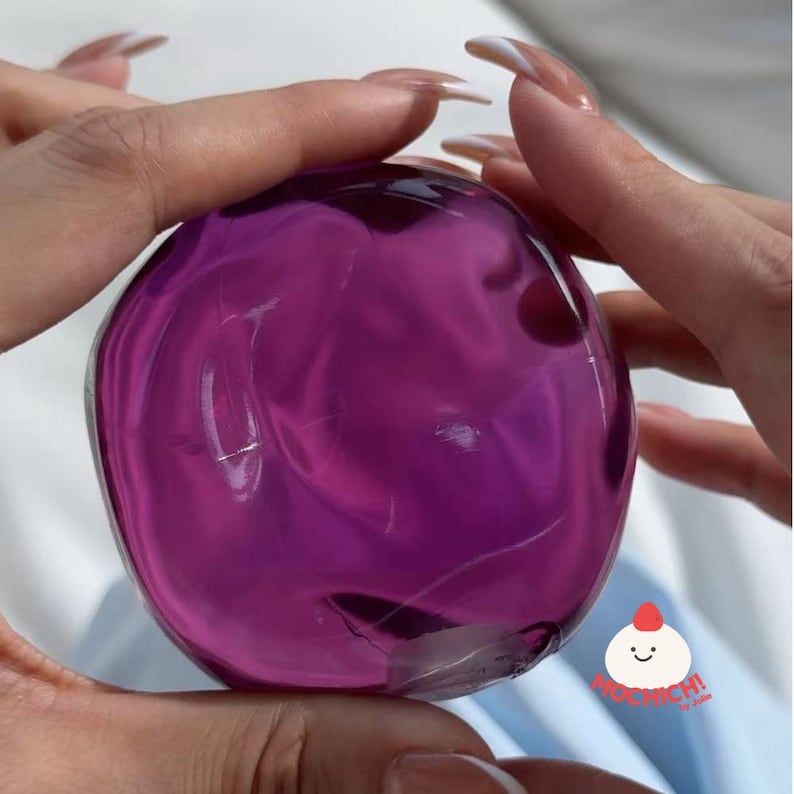 Op de afbeelding: Een doorzichtig, bolvormig object met een dieppaarse tint. De gelachtige bol heeft een glad oppervlak met interne wervelingen. De afbeelding is een close-up, die de textuur en kleur van het object benadrukt.