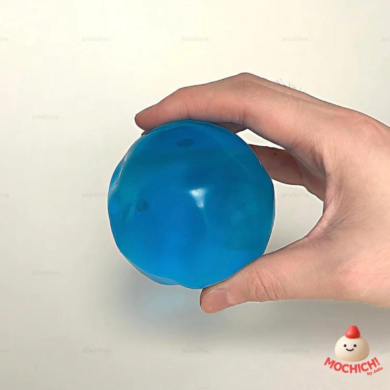 Op de afbeelding: Een helderblauwe stressbal met een glad, glanzend oppervlak, vastgehouden in een hand. De bal heeft een onregelmatige vorm. De achtergrond is effen wit, wat de kleur en vorm van de bal benadrukt.