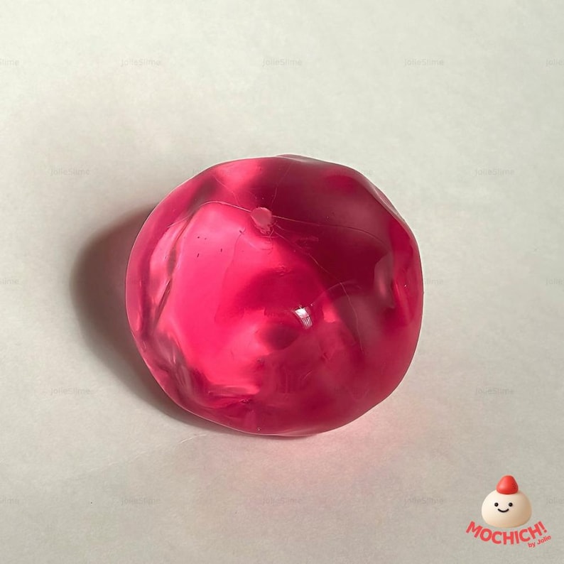 Op de afbeelding: Een doorschijnend, rond, roze object met een enigszins onregelmatige vorm. Het object heeft een glad oppervlak en lijkt gemaakt te zijn van een gelachtig materiaal. De afbeelding staat tegen een witte achtergrond.