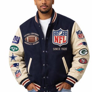 Könnte beinhalten: Marineblaue und cremefarbene Collegejacke mit mehreren NFL-Teamlogos und Aufnähern. Die Jacke hat das NFL-Logo und den Text "SINCE 1920". Die Jacke hat eine Knopfleiste und gestreifte Bündchen und Kragen.