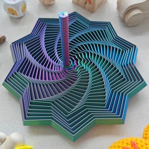 May include: A colorful, geometric wooden toy with a central peg. The toy features layers of blue, green, and purple, creating a spiral effect. Other wooden toys are in the background.