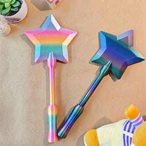 May include: Two star-shaped wands with an iridescent finish. One wand has a rainbow colour scheme, the other is mainly blue and purple. The wands have long, slender handles and are likely toys or decorative items.