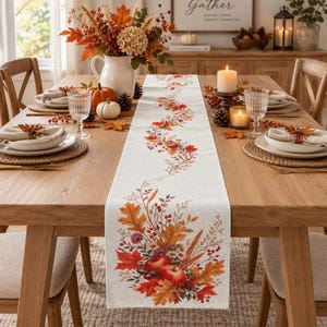 May include: A rectangular off-white table runner featuring a printed design of autumn foliage, including orange and red maple leaves, wheat stalks, red berries, and two red apples at the bottom, with a winding floral pattern extending upwards.