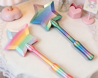 May include: Two star-shaped wands with metallic rainbow finishes. One wand features a gradient transitioning from pink to orange and yellow, while the other displays a gradient of blue, green, and purple. Both have long handles.