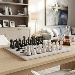 May include: A marble chess set featuring polished black and white stone pieces arranged on a matching square chequered board. The set includes traditional king, queen, bishop, knight, rook, and pawn figures, all crafted with smooth, rounded contours.