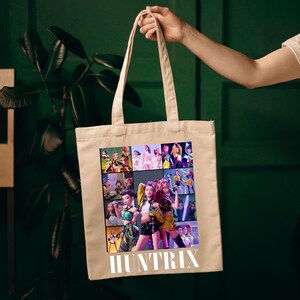 A product mockup showing a vibrant Huntrix Kpop Demon Hunters graphic applied to a physical item. The print highlights the vivid colors and crisp details of the Saja Girls anime PNG design, demonstrating its perfect application for sublimation and DTG printing.