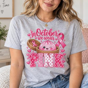 In October We Wear Pink breast cancer awareness PNG featuring a cute pink dumpling in a bamboo steamer, pink ribbon, hearts, bows, sparkles, and polka-dot lettering.