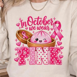 In October We Wear Pink breast cancer awareness PNG featuring a cute pink dumpling in a bamboo steamer, pink ribbon, hearts, bows, sparkles, and polka-dot lettering.