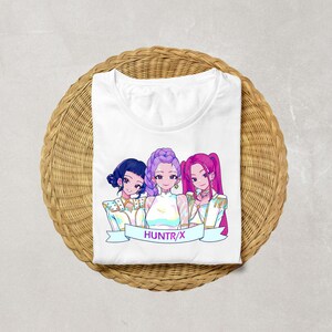 A product mockup showing a vibrant Huntrix Kpop Demon Hunters graphic applied to a physical item. The print highlights the vivid colors and crisp details of the Saja Girls anime PNG design, demonstrating its perfect application for sublimation and DTG printing.