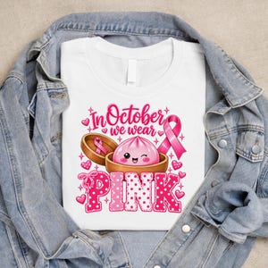 In October We Wear Pink breast cancer awareness PNG featuring a cute pink dumpling in a bamboo steamer, pink ribbon, hearts, bows, sparkles, and polka-dot lettering.