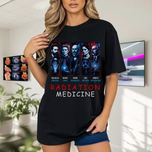 May include: A black t-shirt featuring a graphic print of five historical scientists: Wilhelm Rontgen, Marie Curie, Henri Becquerel, Lise Meitner, and Ernest Rutherford. Below the portraits, the text reads RADIATION MEDICINE in red and white.