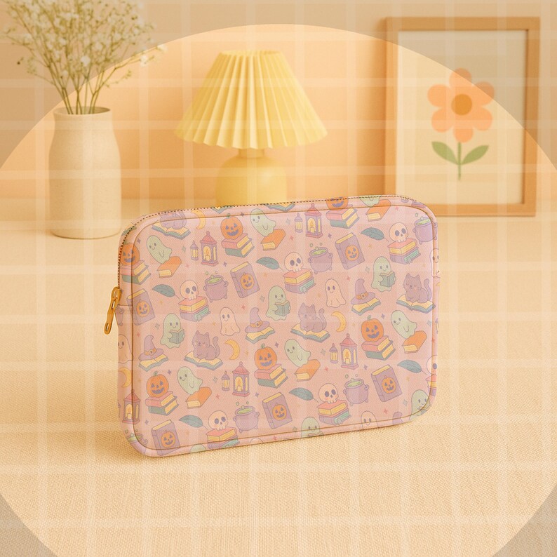May include: A rectangular, pink zippered pouch with a Halloween-themed pattern. The pattern includes ghosts, pumpkins, cats, books, and skulls. The zipper is gold-colored.
