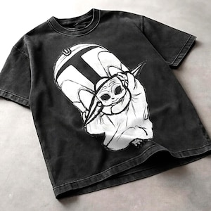 Peut inclure: T-shirt gris fonc&eacute; avec un motif blanc repr&eacute;sentant un personnage de science-fiction. Le motif est une illustration stylis&eacute;e d'une petite cr&eacute;ature extraterrestre. Le t-shirt a un col rond et des manches courtes.